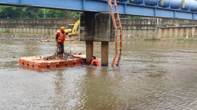 Petugas orange di Kanal Banjir Barat membersihkan aliran sungai. [Suara.com/Fakhri Fuadi]