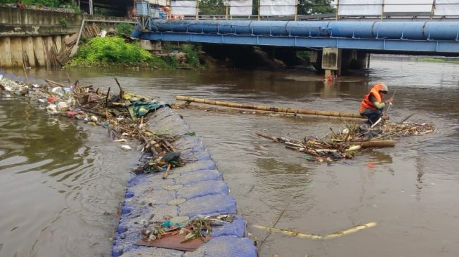 Petugas pasukan oranye tengah membersihkan kali di Banjir Kanal Barat (BKB). (Suara.com/Fakhri Fuadi)