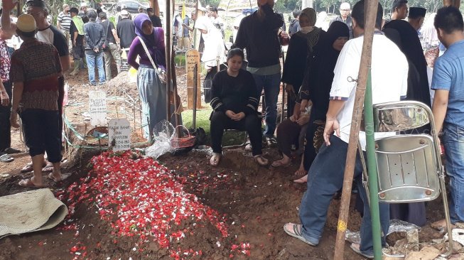 Putri Titian duduk sambil memandangi makam sang ayah. [Wahyu Tri Laksono/Suara.com]