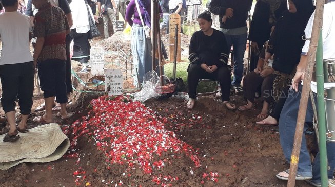 Putri Titian duduk sambil memandangi makam sang ayah. [Wahyu Tri Laksono/Suara.com]