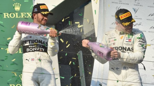 Duet pebalap Mercedes, Lewis Hamilton (kiri) dan Valtteri Bottas, saling menyemprotkan sampanye ke arah masing-masing dalam perayaan kemenangan F1 GP Australia di Sirkuit Albert Park, Minggu (17/3/2019). [AFP/Peter Parks]