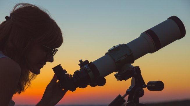 Seorang astronom perempuan sedang mengamati bintang dengan teleskop. [Shutterstock]
