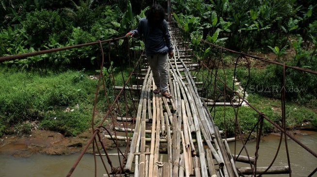 Warga melintasi jembatan gantung yang terbuat dari bambu di Depok, Jawa Barat, Senin (4/8).[Suara.com/Arief Hermawan P]