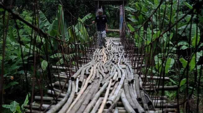 Warga melintasi jembatan gantung yang terbuat dari bambu di Depok, Jawa Barat, Senin (4/8).[Suara.com/Arief Hermawan P]