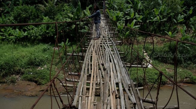 Warga melintasi jembatan gantung yang terbuat dari bambu di Depok, Jawa Barat, Senin (4/8).[Suara.com/Arief Hermawan P]