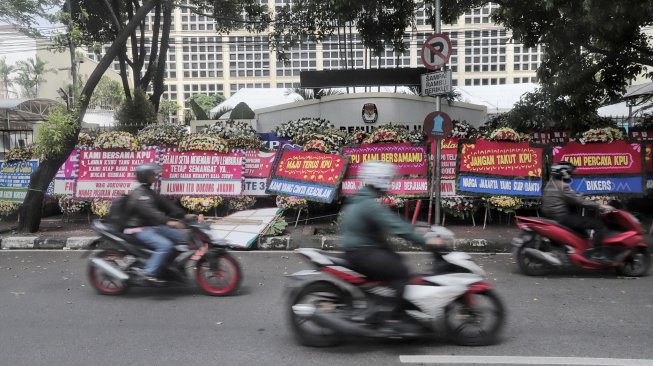 Warga melintas di samping karangan bunga di Kantor KPU, Jakarta, Minggu (21/4). [Suara.com/Muhaimin A Untung]