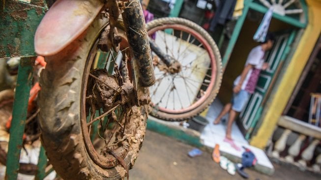 Sebuah sepeda terkena lumpur dengan latar belakang warga berdiri di depan rumahnya pascabanjir yang merendam kawasan Kelurahan Rawajati di Jakarta, Senin (29/4). ANTARA FOTO/Muhammad Adimaja