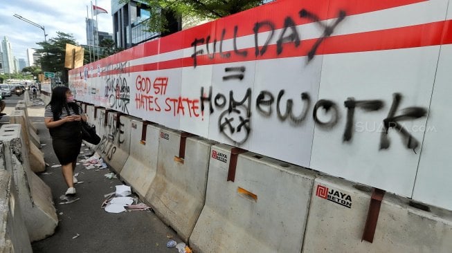 Warga melintas di samping coretan pembatas jalan di kawasan Tosari, Jakarta, Rabu (1/5). [Suara.com/Muhaimin A Untung]
