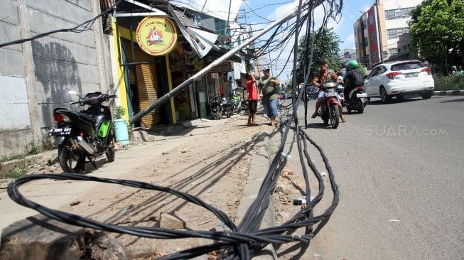 Warga melintasi tiang listrik yang roboh di Jalan Tanjung Duren Raya, Jakarta Barat, (5/2). [Suara.com/Arief Hermawan P]