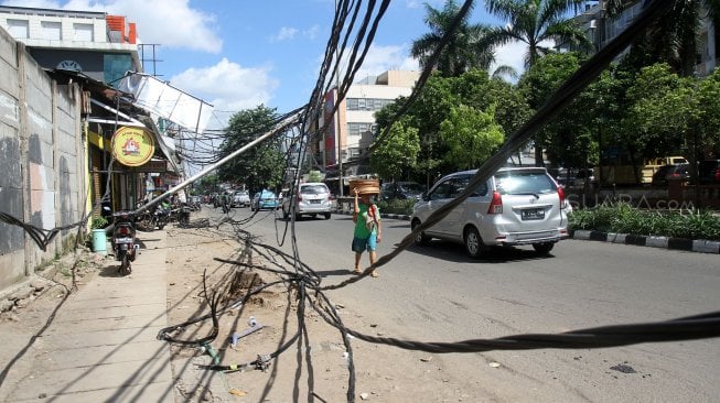 Warga melintasi tiang listrik yang roboh di Jalan Tanjung Duren Raya, Jakarta Barat, (5/2). [Suara.com/Arief Hermawan P]