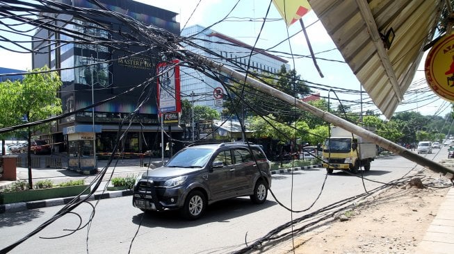 Warga melintasi tiang listrik yang roboh di Jalan Tanjung Duren Raya, Jakarta Barat, (5/2). [Suara.com/Arief Hermawan P]