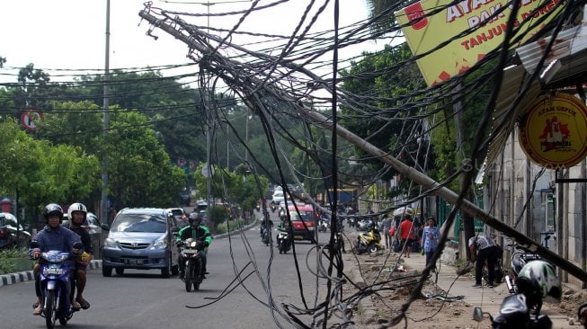 Warga melintasi tiang listrik yang roboh di Jalan Tanjung Duren Raya, Jakarta Barat, (5/2). [Suara.com/Arief Hermawan P]