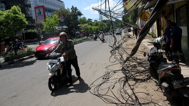 Warga melintasi tiang listrik yang roboh di Jalan Tanjung Duren Raya, Jakarta Barat, (5/2). [Suara.com/Arief Hermawan P]