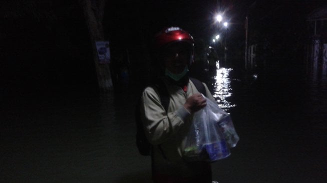 Wawan Wahyudi harus berjalan sepanjang enam ratus meter menerjang banjir untuk membeli bekal makan sahur bersama keluarga, Minggu (5/5/2019). (Suara.com/Tofan Kumara)