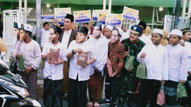 Siswa Madrasah Ibtidaiyah Nahdlatul Ulama (MINU) Trate Putra Gresik membagikan takjil sambil menggunakan topeng wajah tokoh-tokoh Nasional, Sabtu (11/5/2019). (Suara.com/Tofan Kumara)