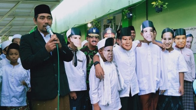 Siswa Madrasah Ibtidaiyah Nahdlatul Ulama (MINU) Trate Putra Gresik membagikan takjil sambil menggunakan topeng wajah tokoh-tokoh Nasional, Sabtu (11/5/2019). (Suara.com/Tofan Kumara)