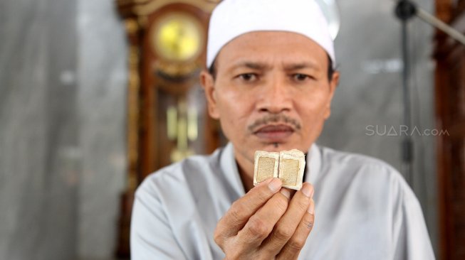 Kyai Tubagus Muhammad Tamyiz menunjukkan Al Quran berukuran mini yang ditulis dengan tinta emas di Masjid Jami Daarussalaam, Pasir Jambu, Kabupaten Bogor, Jawa Barat, Senin (13/5). [Suara.com/Arief Hermawan P]