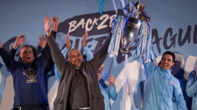 Manajer Manchester City Pep Guardiola (tengah), bersama asisten pelatih Manchester City Mikel Arteta (kanan) dan bek Vincent Kompany (kiri) mengangkat trofi Premier League di depan suporternya di Etihad Stadium. OLI SCARFF / AFP