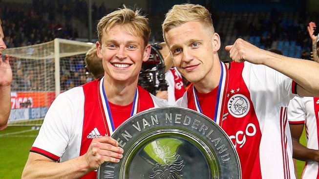 Gelandang Ajax Amsterdam, Frenkie De Jong memegang trofi Liga Belanda bersama Donny van de Beek, usai memastikan raihan gelar juara pasca mengalahkan De Graafschap pada laga pekan ke-34 di Stadion De Vijverberg, Kamis (16/5/2019) dini hari WIB. [Twitter resmi Ajax]