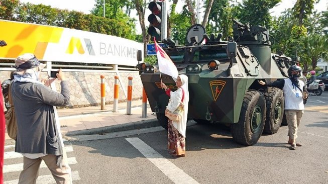 Emak-emak peserta aksi unjuk rasa di kantor Bawaslu Jatim berswafoto di Panser TNI. (Suara,com/Ali)