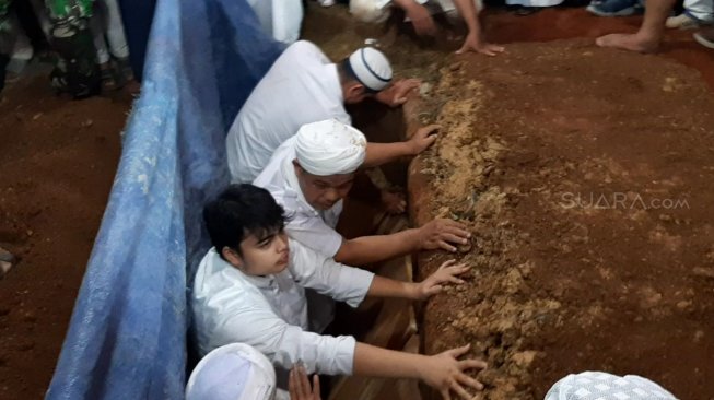 Salah seorang putra almarhum Ustaz Arifin Ilham turun ke liang lahad ikut menguburkan sang ayah. [Suci Febriastuti/Suara.com]