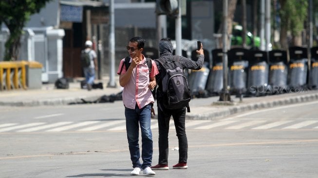 Warga menutupi mata dan hidungnya saat melintas di sekitar gedung Bawaslu, Jalan MH Thamrin, Jakarta, Kamis (23/5). [Suara.com/Arief Hermawan P]