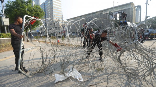 Sejumlah petugas tengah menggulung kawat berduri dan mengangkat barrier beton yang menutupi Jalan MH Thamrin depan kantor Bawaslu, Jakarta, Senin (27/5). [Suara.com/Muhaimin A Untung]