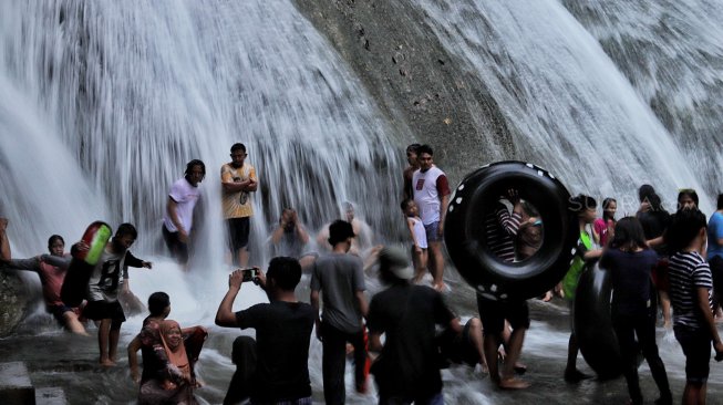 Sejumlah pengunjung menikmati air terjun Bantimurung di objek wisata Bantimurung Maros, Sulawesi Selatan, Jumat (7/6).[Suara.com/Muhaimin A Untung]
