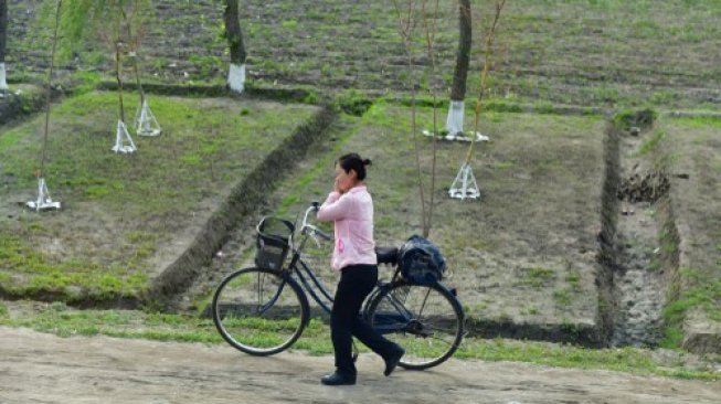 Seorang perempuan di Korea Utara sedang menuntun sepeda sembari berbicara di ponsel. [Shutterstock]