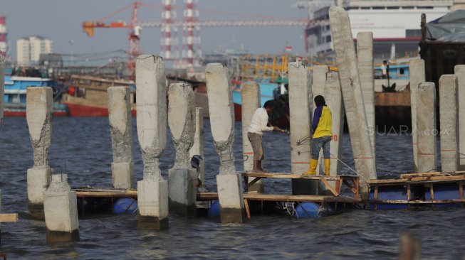 Pekerja menyelesaikan pembangunan dermaga dan pemecah ombak di kawasan Kampung Kerang Hijau, Muara Angke, Jakarta, Rabu (3/7). [Suara.com/Muhaimin A Untung]