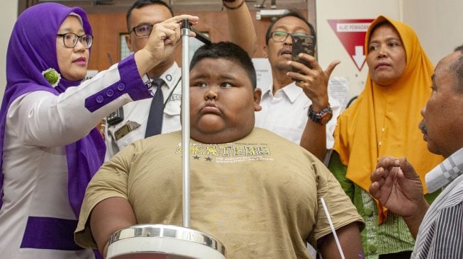 Satia Putra (7) penyandang obesitas dengan berat badan mencapai 101 kg dibantu petugas medis dan kedua orangtuanya mengukur tinggi badan sebelum pemeriksaan medis di Rumah Sakit Umum Daerah (RSUD) Karawang, Karawang, Jawa Barat, Rabu (3/7). [ANTARA FOTO/M Ibnu Chazar]