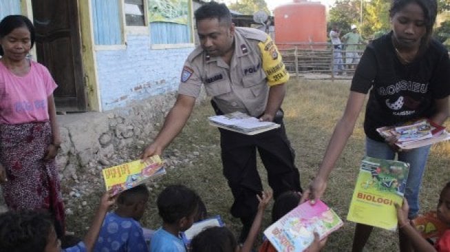 Personel Babinkamtibmas Polsek Kakuluk Mesak Aipda Abraham Doeka (tengah) didampingi seorang guru membagikan buku pelajaran dan buku bacaan kepada sejumlah anak di Desa Kabulak, Kecamatan Kakuluk Mesak, Kabupaten Belu, NTT, Selasa (9/7/2019). Selain bertugas sebagai Babinkamtibmas, Aipda Abraham Doeka juga melatih anak-anak yang putus sekolah untuk belajar membaca dan menulis di desa  ini [ANTARA FOTO/Kornelis Kaha/wsj].