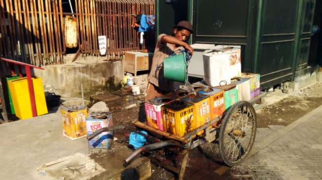Agus Mulyono (35) pedagang air di Kota Lama Semarang sedang menuangkan air ke dalam kaleng bekas yang diambil dari sumur tua bersejarah peninggalan penjajahan Belanda, Kamis (11/7/2019). [Suara.com/Adam Iyasa]