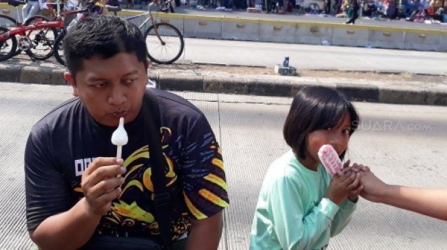 Warga yang tengah asyik menikmati es krim gratis dari Joyday di Hari Es Krim Sedunia di area Car Free Day, depan Patung Jenderal Sudirman, Dukuh Atas, Jakarta, Minggu (21/7/2019). (Suara.com/Risna Halidi) 