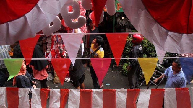 Pengunjung melintasi bendera dan umbul-umbul yang dipajang pedagang di pintu barat Pasar Jatinegara, Jakarta, Selasa (30/7). [Suara.com/Arief Hermawan P]