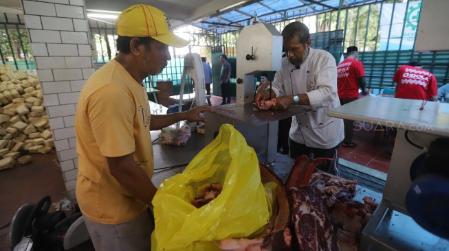 Petugas panitia hewan kurban memasukkan daging sapi ke besek bambu di Masjid Istiqlal, Jakarta, Minggu (11/8). [Suara.com/Arya Manggala]