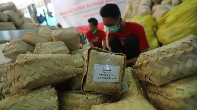 Petugas panitia hewan kurban memasukkan daging sapi ke besek bambu di Masjid Istiqlal, Jakarta, Minggu (11/8). [Suara.com/Arya Manggala]