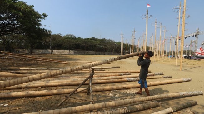 Pekerja memasang bendera merah putih pada pohon pinang untuk acara panjat pinang kolosal di kawasan Ancol, Jakarta, Rabu (14/8). [Suara.com/Arya Manggala]