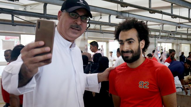 Seorang lelaki berselfie dengan tukang daging Mohammad Ibraheem yang mirip dengan pemain Liverpool Mohamed Salah di rumah jagal hewan di Kota Kuwait, Selasa [13/8]. [AFP Photo/ Yasser Al-Zayyat]
