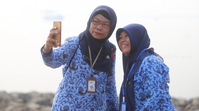 Sejumlah ASN (Aparatur Sipil Negara) Selfie di pinggir pantai usai mengikuti upacara peringatan hari kemerdekaan di Pulau D Reklamasi, Jakarta Utara, Sabtu (17/8). [Suara.com/Arya Manggala]