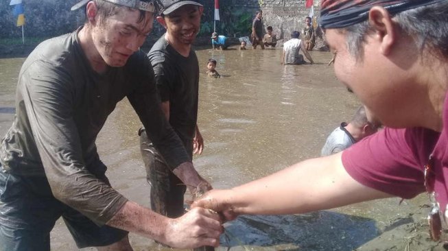 Seorang bule asal Belgia berhasil mendapat seekor lele saat mengikuti lomba tangkap ikan tersebut di Desa Kemutug Lor, Kabupaten Banyumas, Jawa Tengah, Sabtu (17/8/2019). [Suara.com/Teguh Lumbiria]