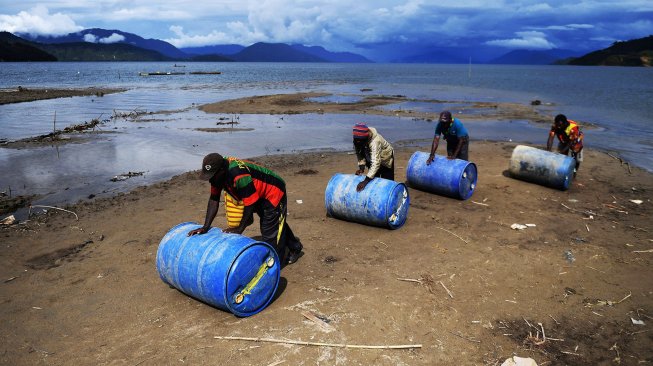 Pekerja mendorong drum berisi BBM yang dibawa melintasi Danau Paniai setibanya di Kampung Obano, Distrik Paniai Barat, Papua, Kamis (29/11/2018).