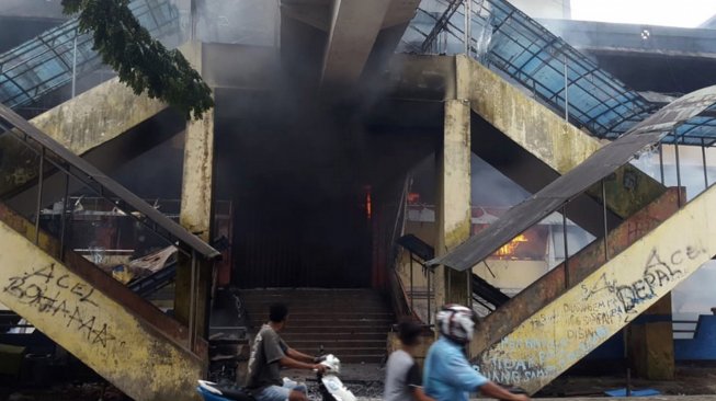 Warga melintasi Pasar Tambruni yang dibakar massa saat melakukan aksi di Kabupaten Fakfak, Papua Barat, Rabu (21/8). [ANTARA FOTO/Wahyu Rumagesan]