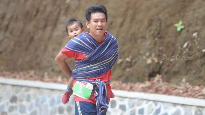 Lorenso Sutanto menggendong anaknya saat mengikuti lomba lari Situ Gunung Trail Run (SGTR) 2019 di Situ Gunung, Sukabumi, Jawa Barat, Minggu (25/8). [Suara.com/Arya Manggala]