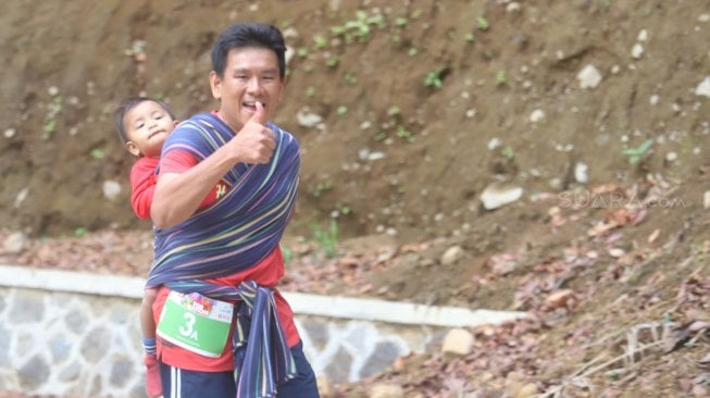 Lorenso Sutanto menggendong anaknya saat mengikuti lomba lari Situ Gunung Trail Run (SGTR) 2019 di Situ Gunung, Sukabumi, Jawa Barat, Minggu (25/8). [Suara.com/Arya Manggala]