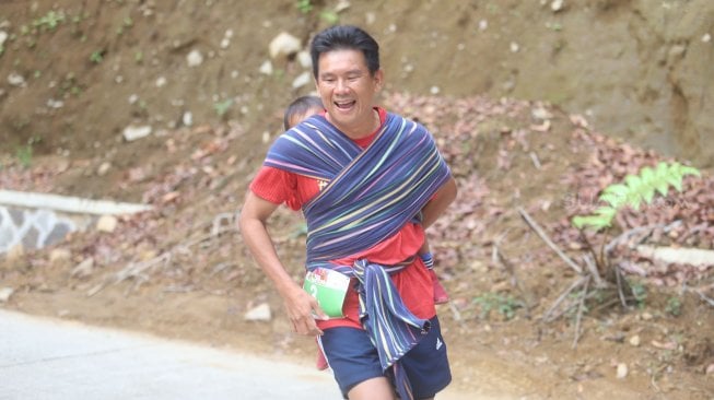 Lorenso Sutanto menggendong anaknya saat mengikuti lomba lari Situ Gunung Trail Run (SGTR) 2019 di Situ Gunung, Sukabumi, Jawa Barat, Minggu (25/8). [Suara.com/Arya Manggala]