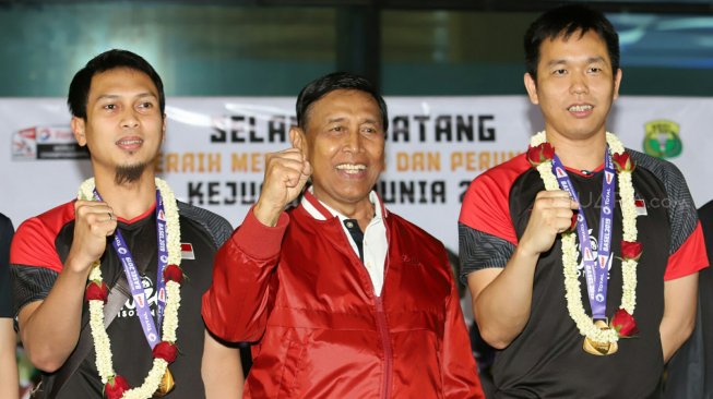 Ketua Umum PBSI Wiranto berfoto bersama pebulutangkis ganda putra Indonesia, Hendra Setiawan dan Mohammad Ahsan menunjukan medali emas di Terminal 3, Bandara Soekarno Hatta, Tangerang, Banten, Selasa (27/8).[Suara.com/Arya Manggala]