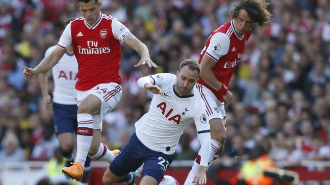 Gelandang serang Tottenham Hotspur, Christian Eriksen terjatuh usai dihadang dua pemain Arsenal pada lanjutan Liga Primer Inggris 2019/20 antara Tottenham Hotspur vs Arsenal, Minggu (1/9/2019). (Ian KINGTON / IKIMAGES / AFP)