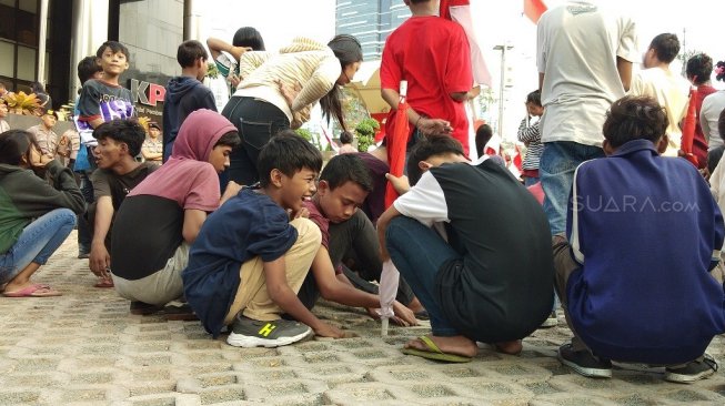 Bocah yang ikut aksi dukung Revisi UU KPK terlihat asik main pasir di konblok bolong di depan Gedung KPK. (Suara.com/Ria Rizki)