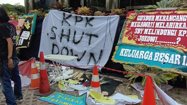 Kain spanduk bertulisan "KPK Shut Down" di antara sejumlah karangan bunga di depan Gedung KPK, Jumat (13/9/2019) pagi, sebelum akhirnya porak-poranda usai demo ricuh massa pendukung revisi UU KPK pada sore harinya. [Suara.com / Arsito Hidayatullah]